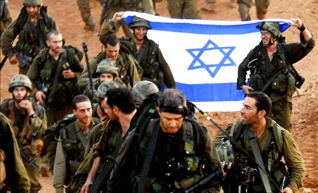 Israeli soldiers hold an Israeli flag as they walk together after leaving Lebanon near the Israeli-Lebanon border