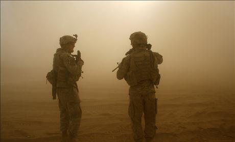 A U.S. soldier stand walk in a cloud of dust as a Blackhawk helicopter takes off during a mission in southern Baghdad