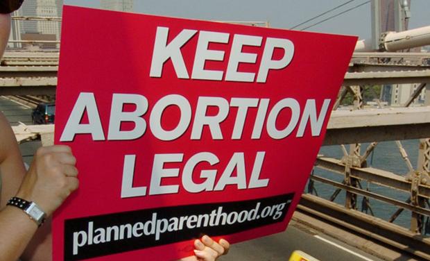 Planned Parenthood abortion rights protester signals Brooklyn Bridge traffic.