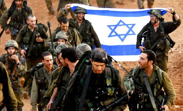 Israeli soldiers hold an Israeli flag as they walk together after leaving Lebanon near the Israeli-Lebanon border