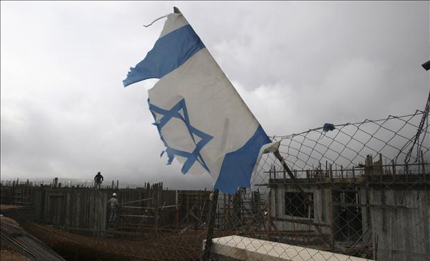 An Israeli national flag is seen as Palestinian labourers work on a building under construction in the Jewish settlement of Har Gilo