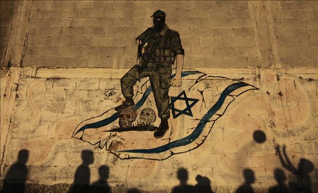The shadows of Palestinian children are cast against a wall as they play with a ball in front of an anti-Israel mural in Gaza City
