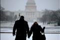 A couple walk through the snow in front of the Capitol Building on the Washington Mall